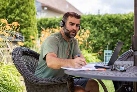 ARO College man taking the landscape construction management course on computer in a garden with headphones on