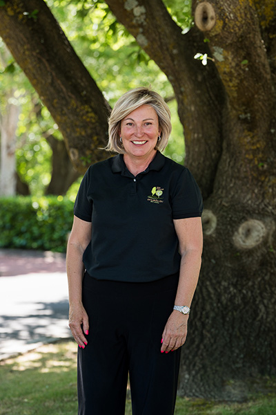Judy Parkes Chief Operating Officer ARO College standing in official polo shirt infront of a tree